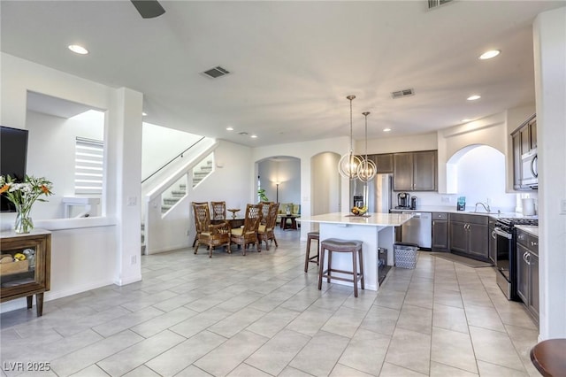 kitchen featuring arched walkways, appliances with stainless steel finishes, a center island, a kitchen bar, and visible vents