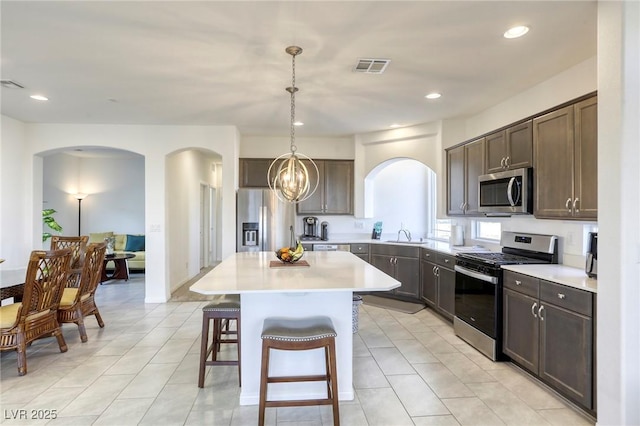 kitchen with arched walkways, a breakfast bar area, stainless steel appliances, a kitchen island, and dark brown cabinets