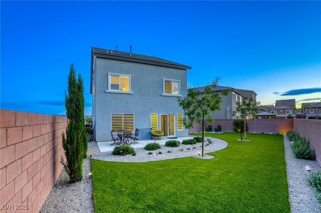 rear view of house with a fenced backyard, stucco siding, a patio area, and a lawn