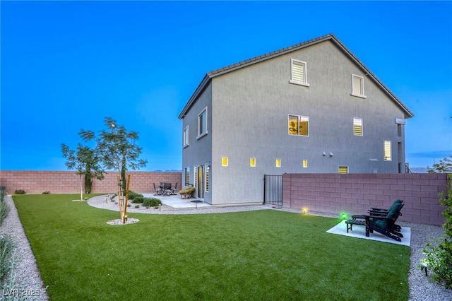 rear view of property with a patio, a lawn, stucco siding, and a fenced backyard