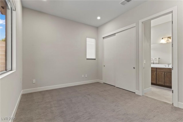 unfurnished bedroom featuring light colored carpet, ensuite bath, visible vents, recessed lighting, and baseboards