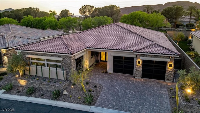 mediterranean / spanish home featuring a tiled roof, a garage, stone siding, and decorative driveway