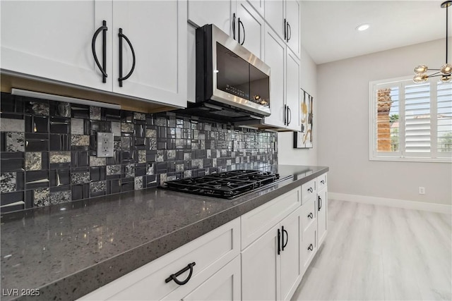 1185 Via Casa Palermo, Henderson, NV 89011 - kitchen featuring white cabinets, black gas cooktop, stainless steel microwave, baseboards, and decorative backsplash