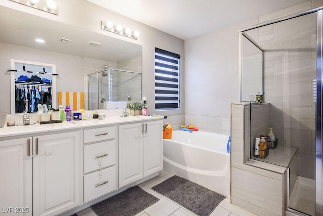 bathroom featuring double vanity, a stall shower, a spacious closet, tile patterned floors, and a garden tub