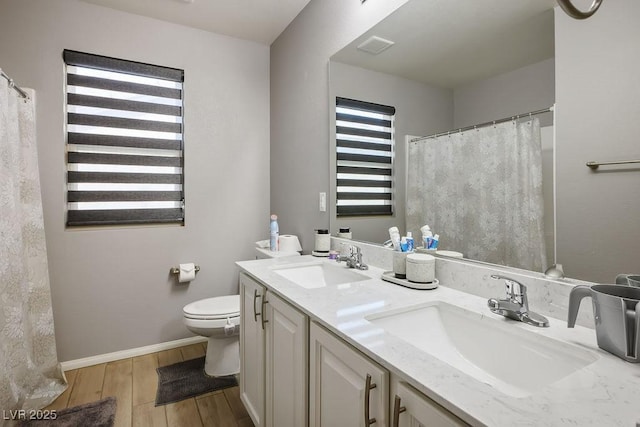 full bath featuring toilet, wood finished floors, double vanity, and a sink