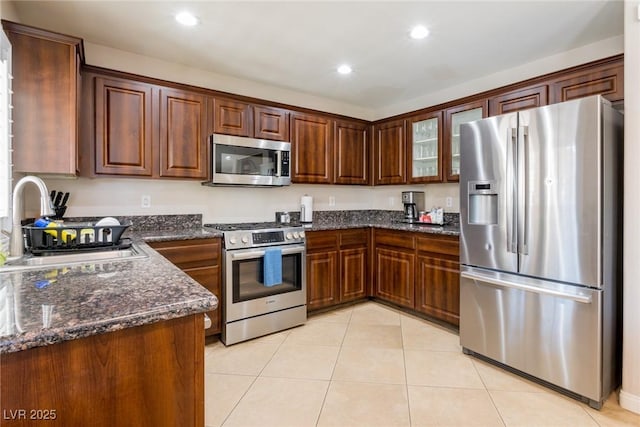 kitchen with light tile patterned floors, a sink, appliances with stainless steel finishes, recessed lighting, and dark stone counters