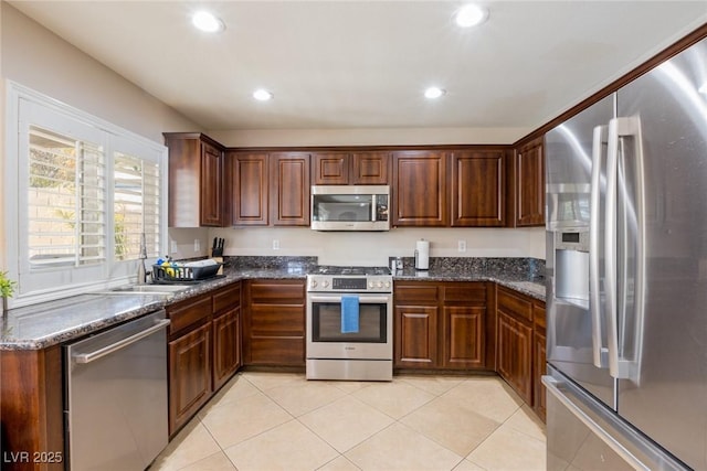 kitchen with dark stone counters, light tile patterned floors, recessed lighting, a sink, and stainless steel appliances