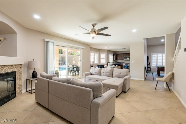 living area featuring baseboards, recessed lighting, light tile patterned floors, a tiled fireplace, and ceiling fan