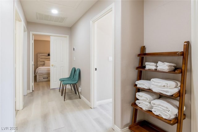 hall featuring visible vents, baseboards, and light wood-type flooring