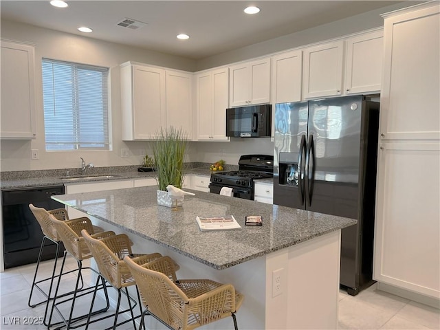 kitchen featuring light tile patterned floors, white cabinetry, visible vents, black appliances, and a sink