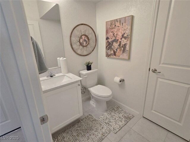 half bathroom with baseboards, tile patterned floors, vanity, and toilet