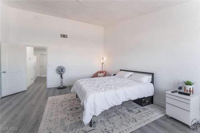 bedroom featuring visible vents, baseboards, wood finished floors, and a textured ceiling