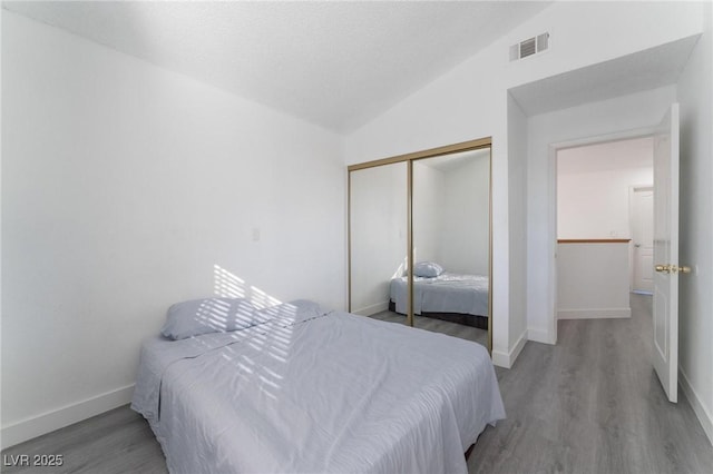 bedroom with visible vents, baseboards, a closet, wood finished floors, and lofted ceiling