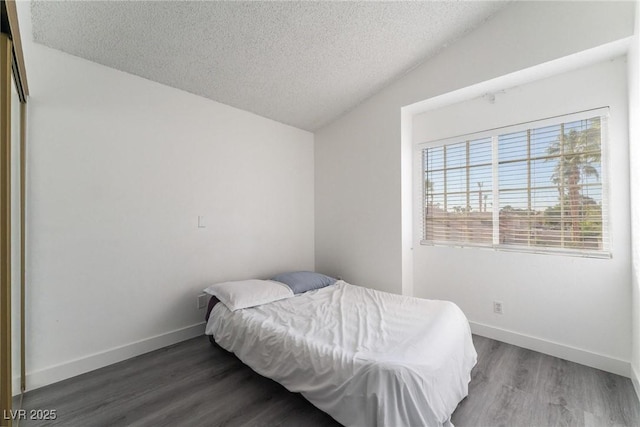 bedroom with baseboards, wood finished floors, vaulted ceiling, and a textured ceiling