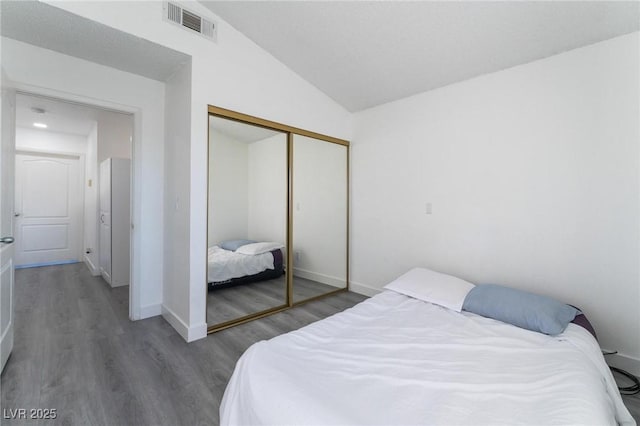 bedroom featuring a closet, baseboards, visible vents, lofted ceiling, and wood finished floors