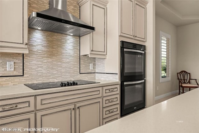 kitchen featuring wall chimney range hood, light countertops, black appliances, and backsplash