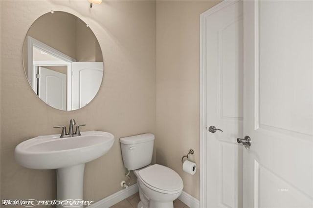 half bathroom featuring toilet, baseboards, and tile patterned floors