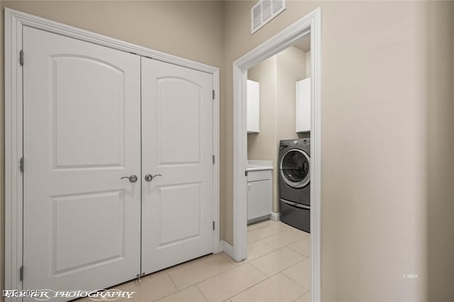 washroom with baseboards, light tile patterned flooring, visible vents, washer / dryer, and cabinet space