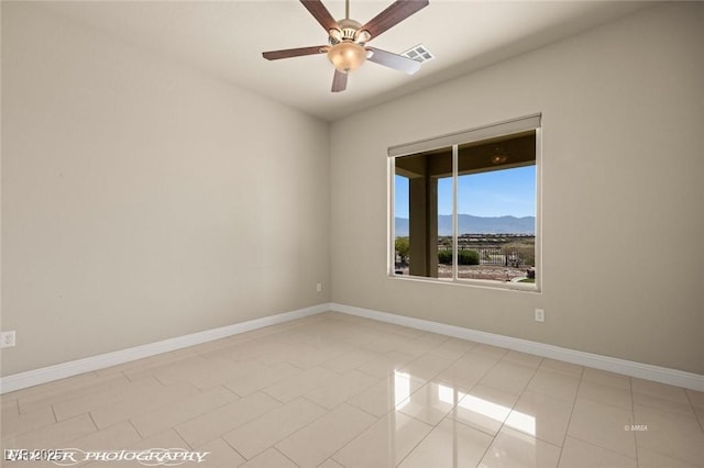 empty room with a ceiling fan, a mountain view, baseboards, light tile patterned floors, and visible vents