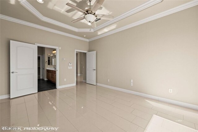 unfurnished bedroom with a tray ceiling, crown molding, ensuite bath, and baseboards