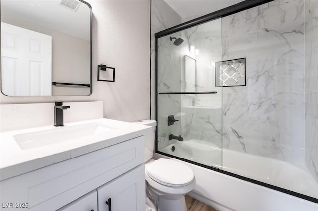 bathroom with vanity, enclosed tub / shower combo, a textured wall, toilet, and visible vents