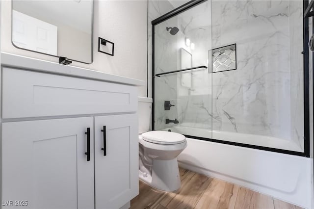 bathroom featuring toilet, wood finished floors, vanity, and enclosed tub / shower combo