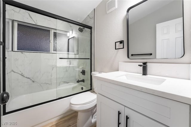 full bath with vanity, visible vents, toilet, bath / shower combo with glass door, and a textured wall