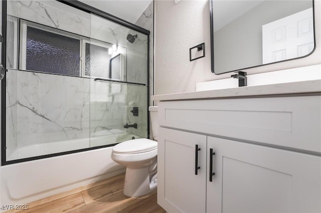 full bathroom featuring shower / bath combination with glass door, vanity, a textured wall, toilet, and wood finished floors