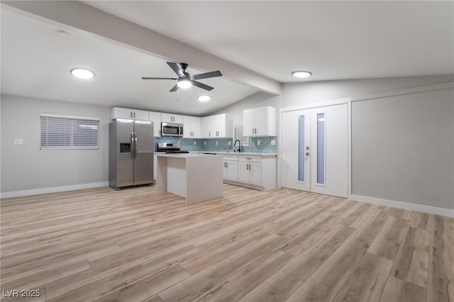 kitchen with a center island, a sink, appliances with stainless steel finishes, white cabinetry, and vaulted ceiling with beams
