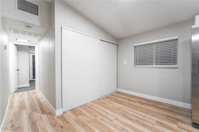 unfurnished bedroom with visible vents, light wood-type flooring, a closet, and lofted ceiling