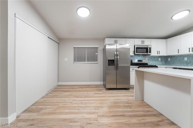 kitchen featuring light countertops, appliances with stainless steel finishes, white cabinetry, backsplash, and light wood-style flooring