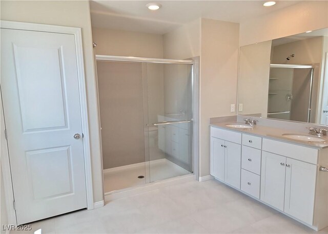 full bathroom featuring a stall shower, double vanity, a sink, and baseboards