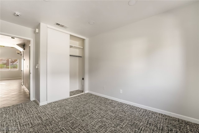 unfurnished bedroom with a closet, baseboards, tile patterned flooring, visible vents, and carpet