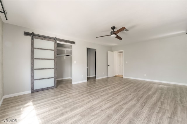 unfurnished bedroom with visible vents, baseboards, a barn door, a ceiling fan, and light wood-style floors