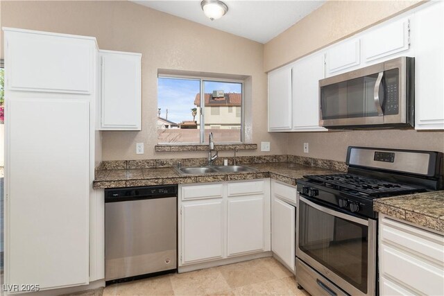 kitchen with appliances with stainless steel finishes, white cabinets, tile countertops, and a sink
