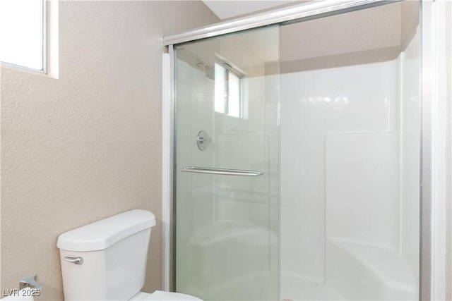 bathroom featuring toilet, a stall shower, a textured wall, and a wealth of natural light