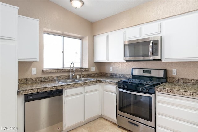 kitchen featuring appliances with stainless steel finishes, white cabinets, a textured wall, a sink, and tile countertops