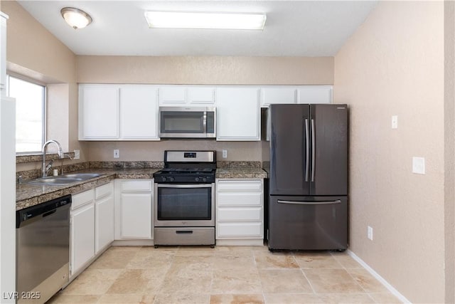 kitchen featuring appliances with stainless steel finishes, white cabinetry, baseboards, and a sink