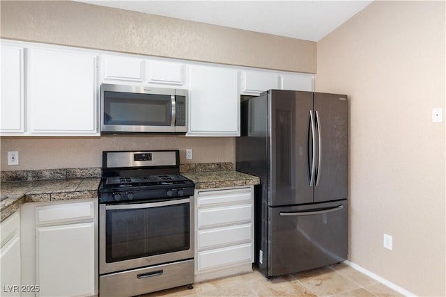kitchen featuring white cabinetry, baseboards, tile countertops, and appliances with stainless steel finishes