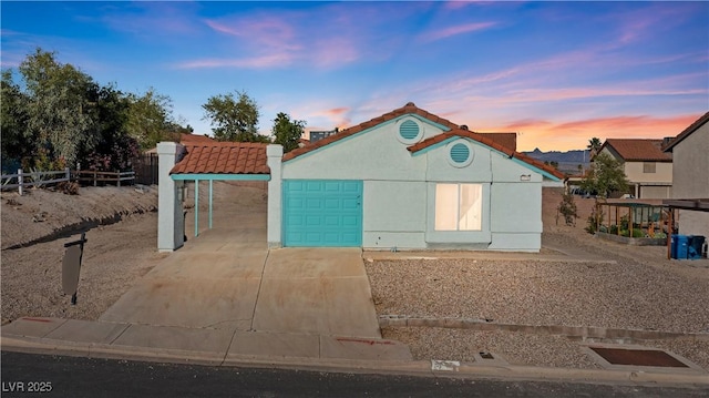 view of front of home with concrete driveway, a tiled roof, stucco siding, fence, and a garage