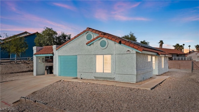 back of house with driveway, roof mounted solar panels, stucco siding, an attached garage, and fence