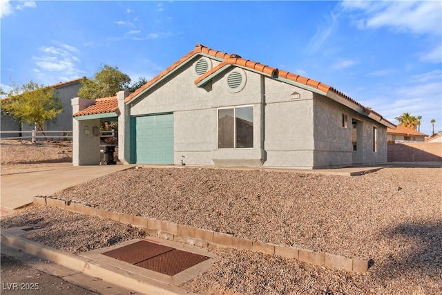 view of front facade with a tile roof, a garage, concrete driveway, stucco siding, and fence