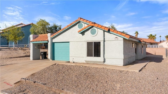 view of front of home with driveway, a tile roof, stucco siding, fence, and a garage