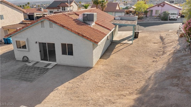 back of house featuring central AC, a residential view, a tiled roof, and stucco siding