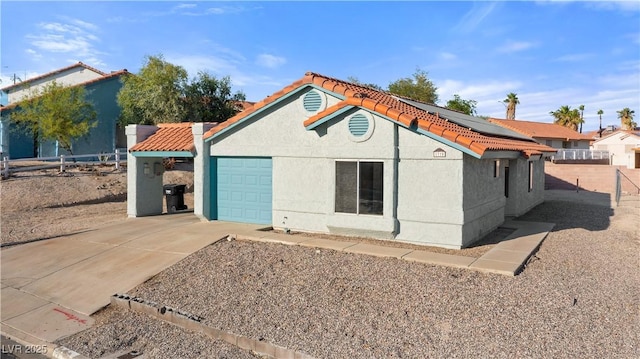 view of front of property featuring stucco siding, fence, solar panels, driveway, and an attached garage