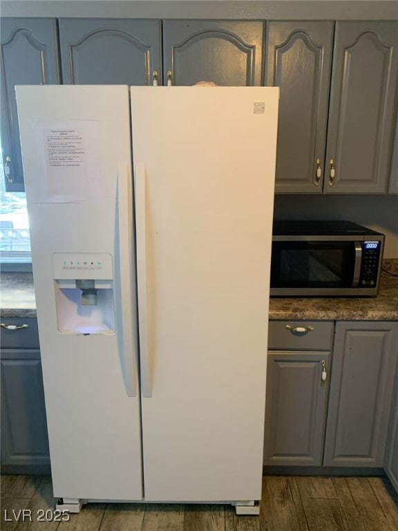kitchen with gray cabinets, stainless steel microwave, white fridge with ice dispenser, and dark wood-style flooring