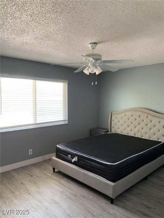 bedroom featuring ceiling fan, a textured ceiling, light wood finished floors, and baseboards