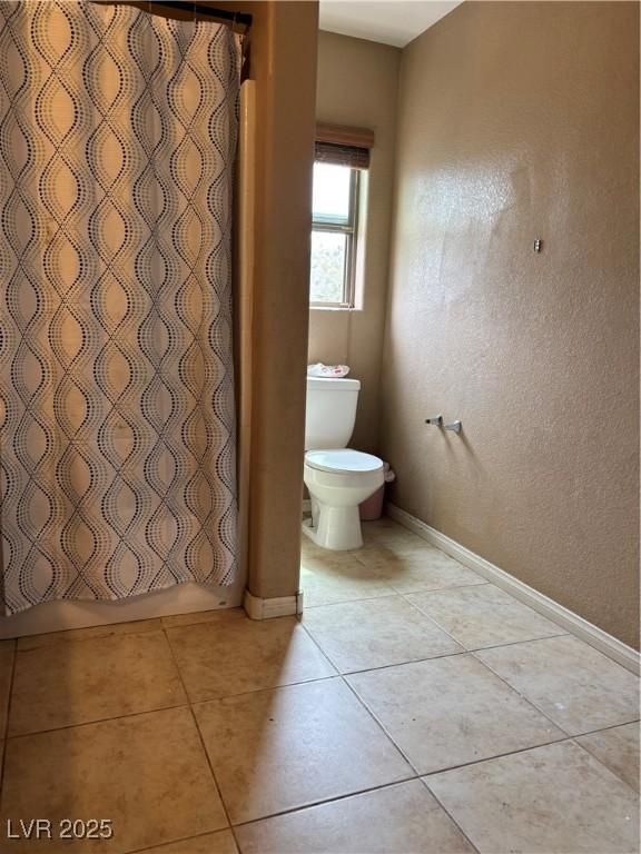 bathroom featuring toilet, baseboards, a shower with shower curtain, and tile patterned flooring