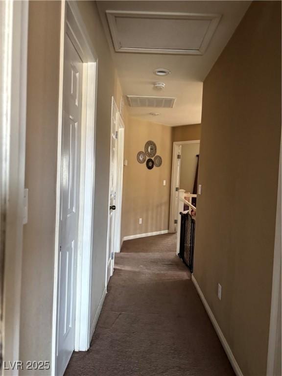 corridor featuring visible vents, baseboards, carpet flooring, and attic access