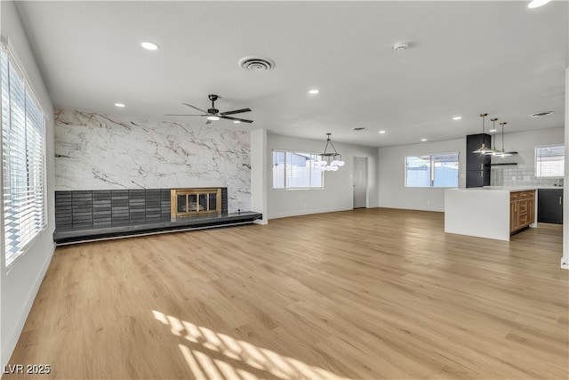 unfurnished living room with recessed lighting, visible vents, light wood finished floors, ceiling fan with notable chandelier, and a premium fireplace